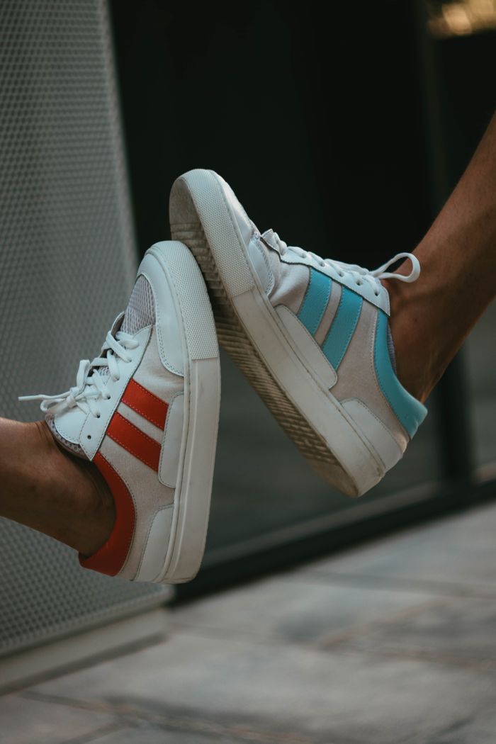 Side view of crop anonymous people wearing sportive sneakers with white laces on blurred background of building